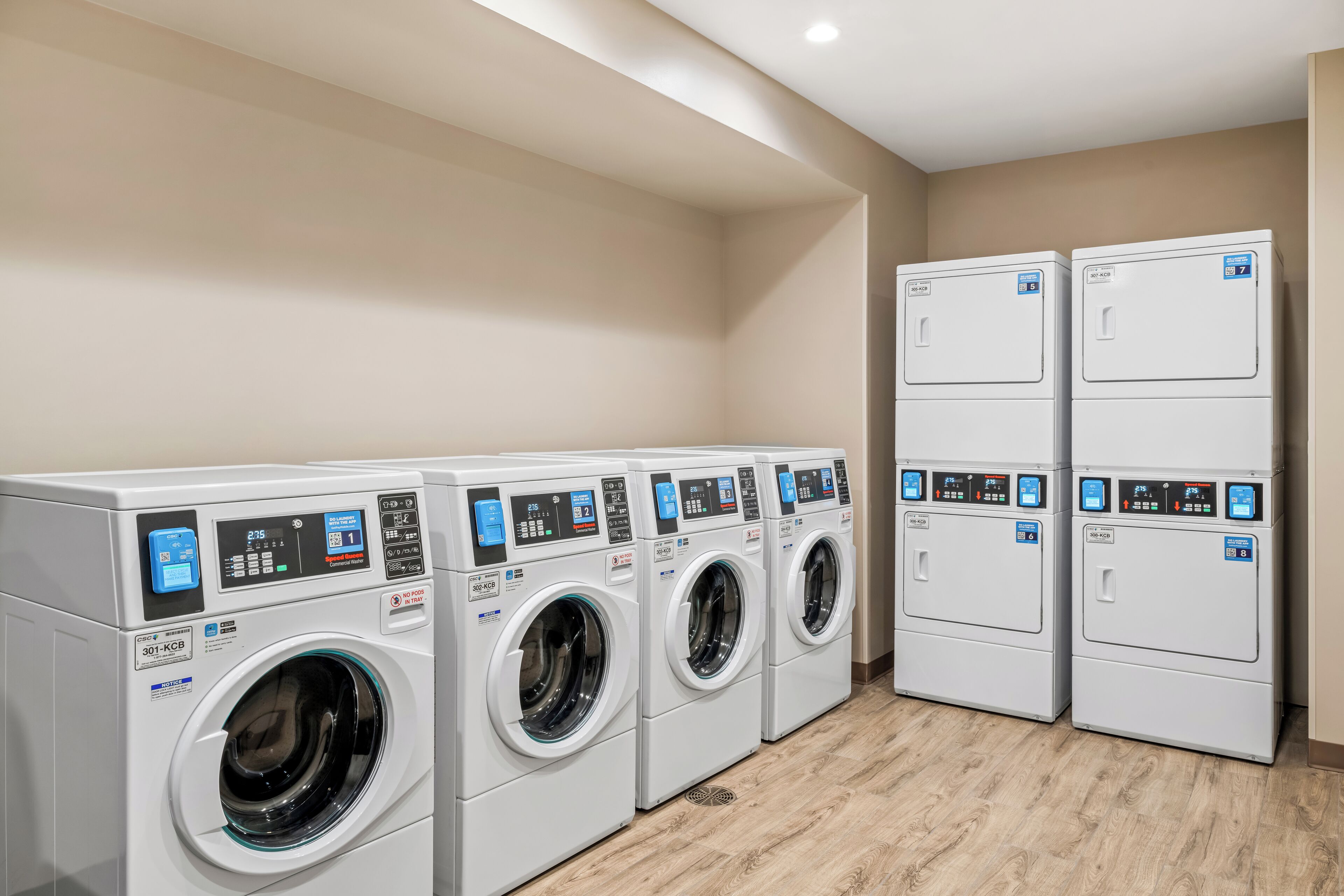 A laundry room with four front-loading washing machines and two stacked dryers.