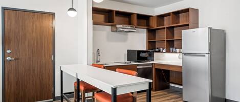 A modern kitchen with a white countertop, stainless steel appliances, and wooden shelving.