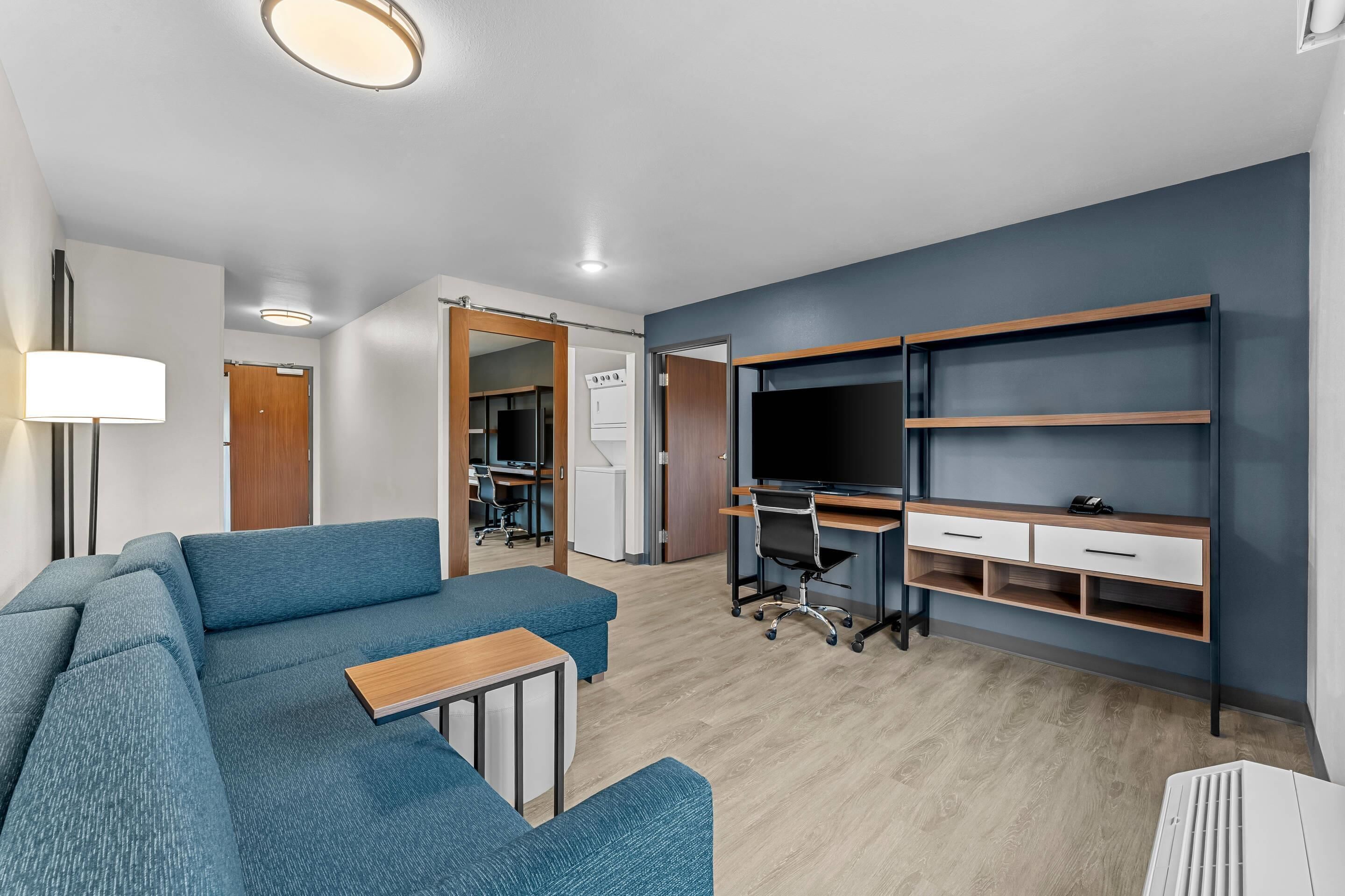 A modern living room with a sectional sofa, a desk with a computer, a TV, and built-in shelving.