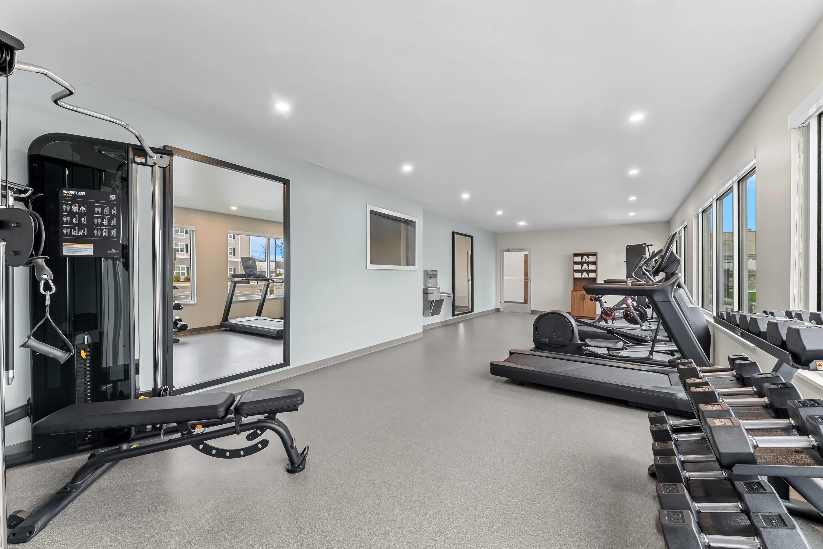Une salle de sport équipée de matériel d’exercice, d’un banc, de tapis de course et d’un miroir.