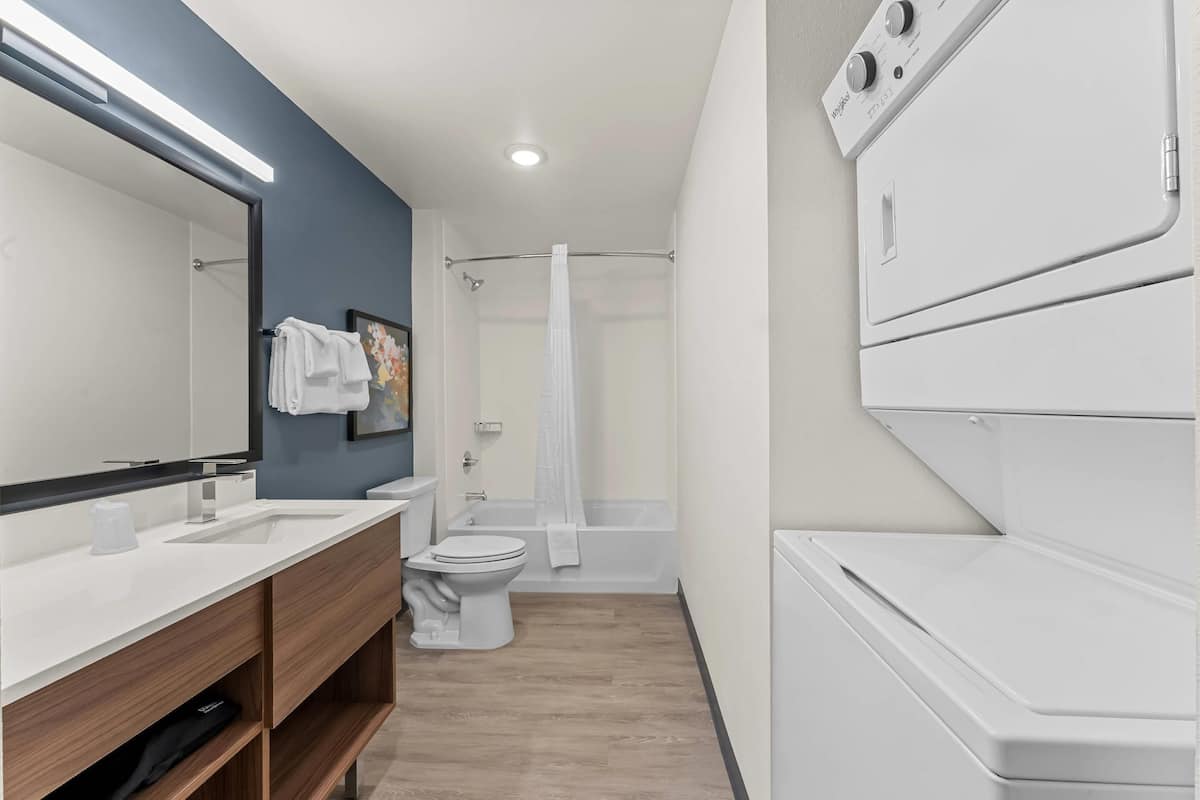 A modern bathroom with a sink, toilet, bathtub, and a stacked washer and dryer.