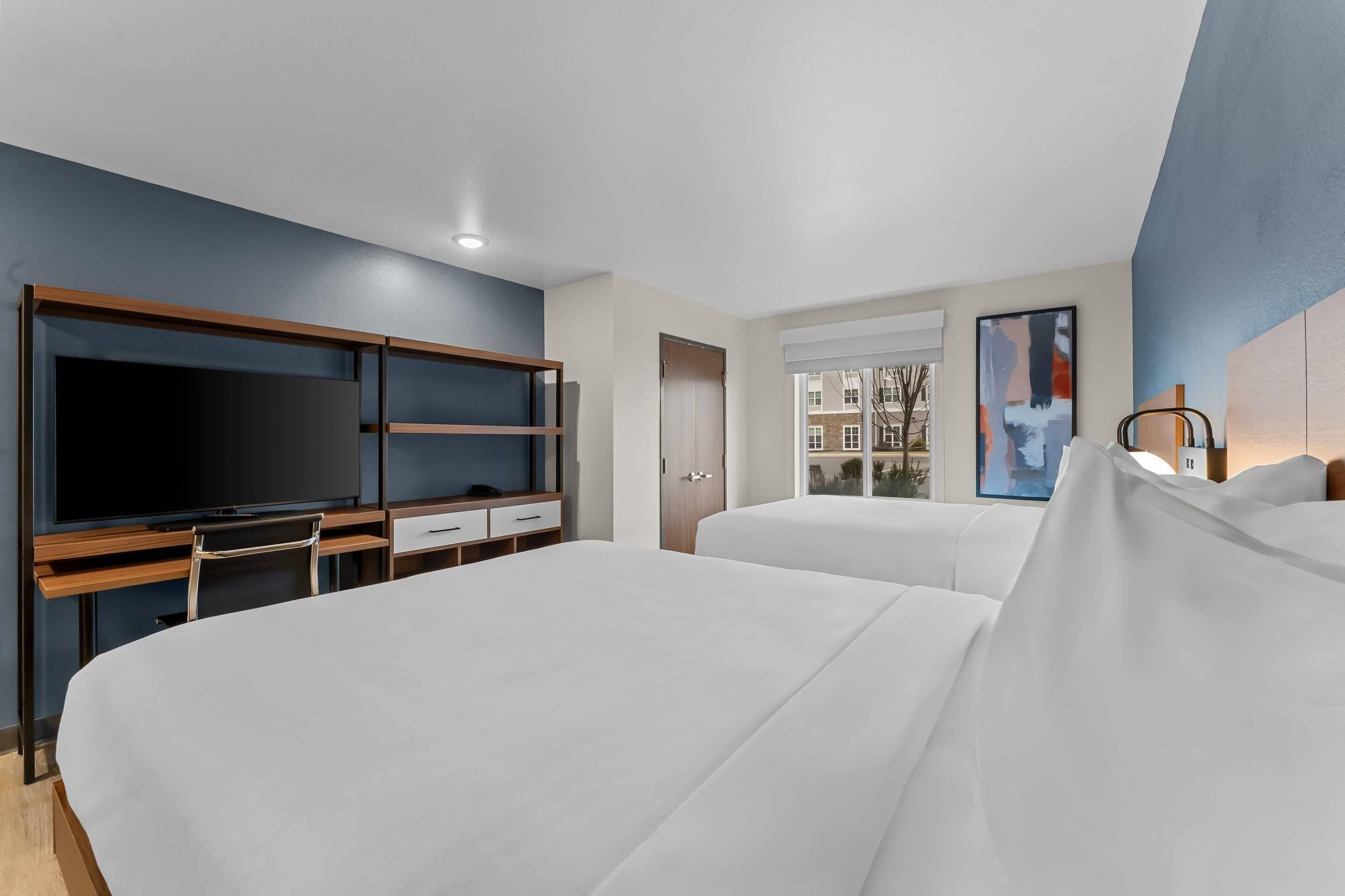 Hotelkamer met een groot bed, een televisie, een bureau met lades en een raam met uitzicht op gebouwen.