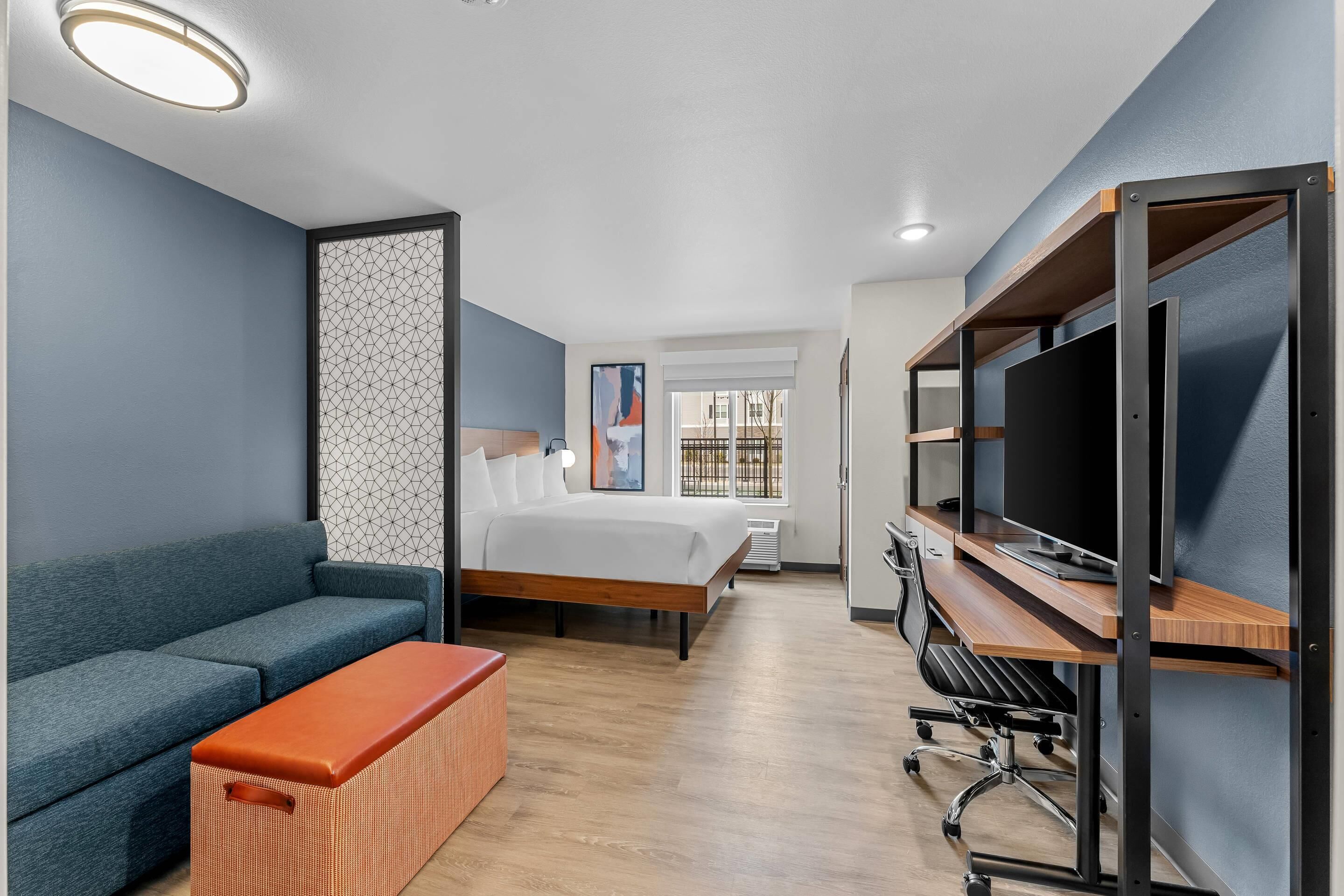 A hotel room with a bed, a sofa, a TV stand, and a desk.