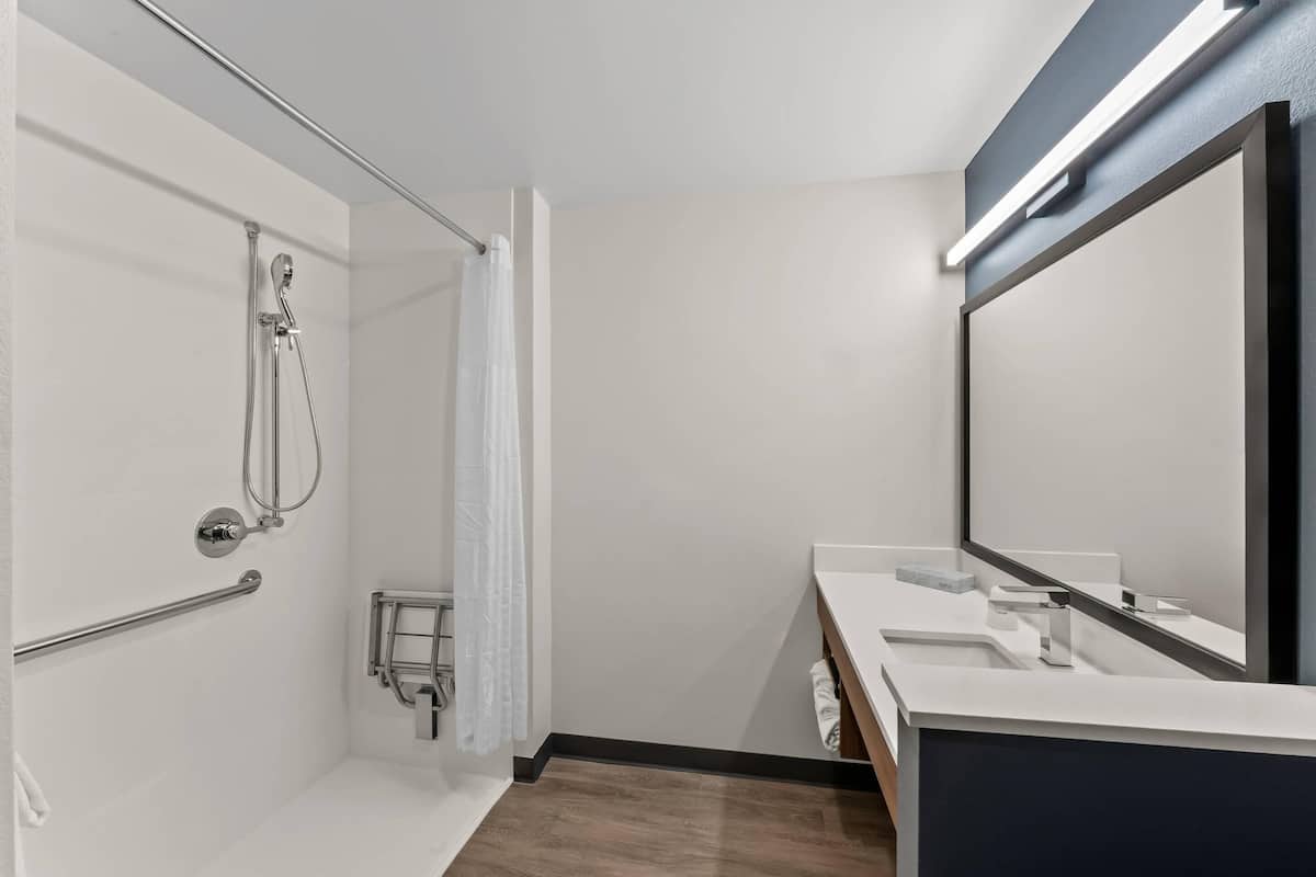 A modern bathroom with a shower, a handrail, a towel rack, a mirror, and a sink.