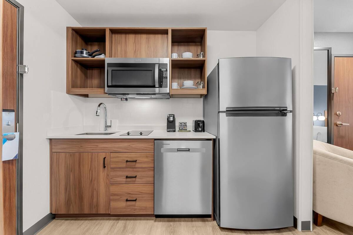 A compact kitchen with a microwave, refrigerator, dishwasher, and wooden cabinets.