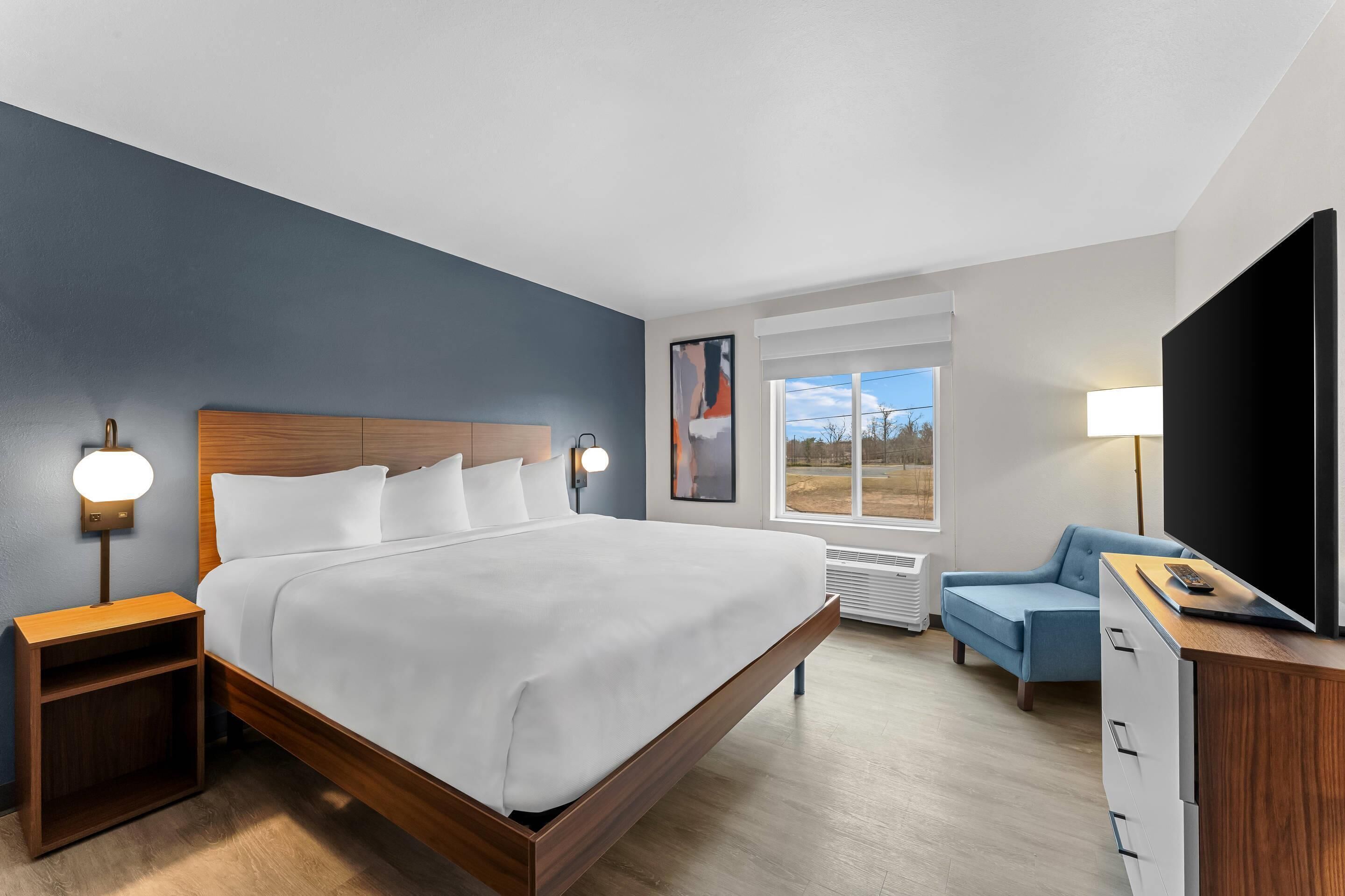A hotel room with a bed, bedside tables, a TV, a desk, and a window.