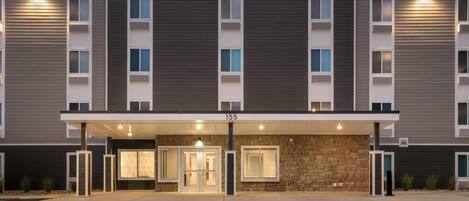 A hotel entrance with a modern design, featuring a large sign for Woodspring Suites, a covered entrance, and a stone facade.