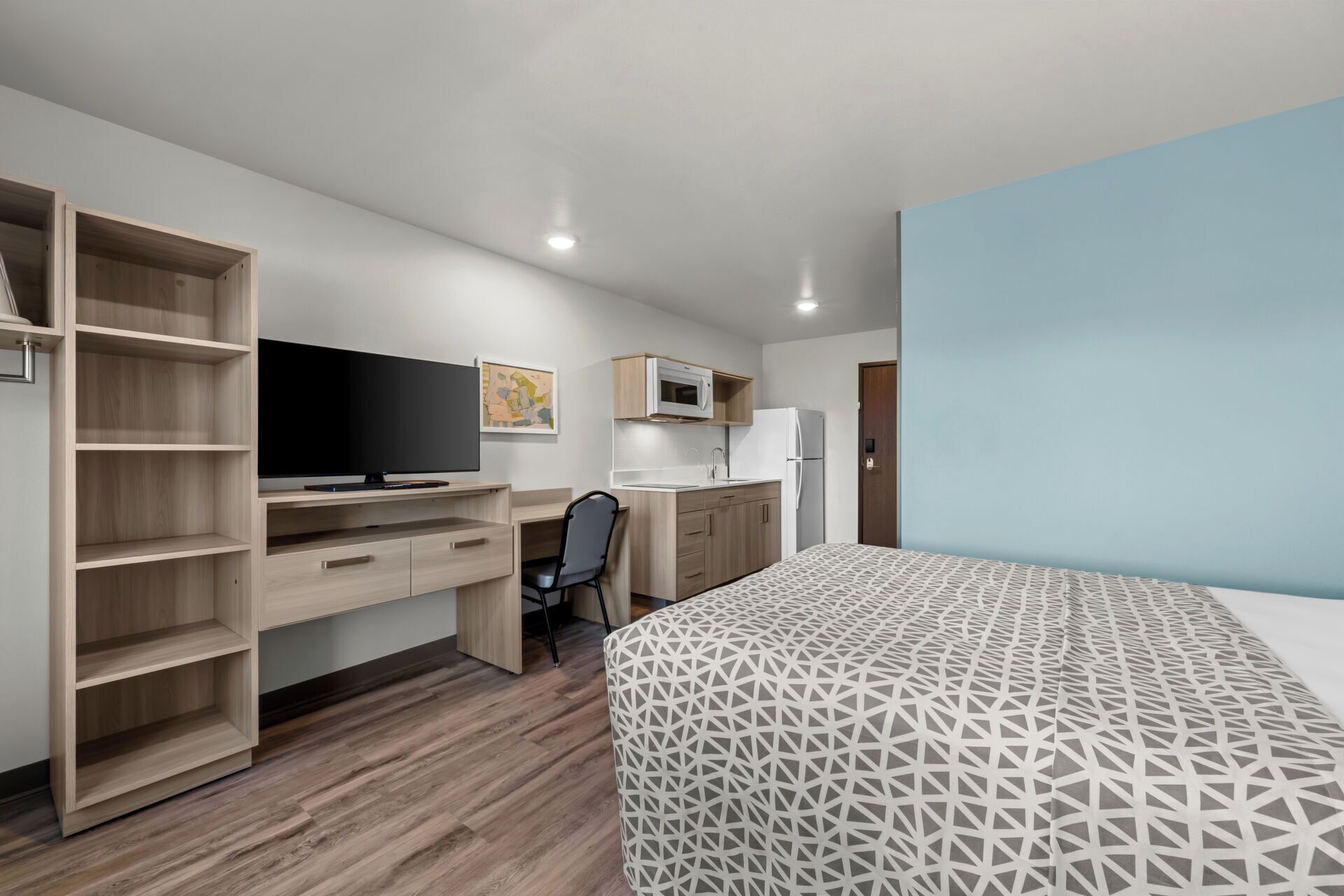 A bedroom with a bed, a desk, a chair, a TV, a microwave, and a refrigerator.
