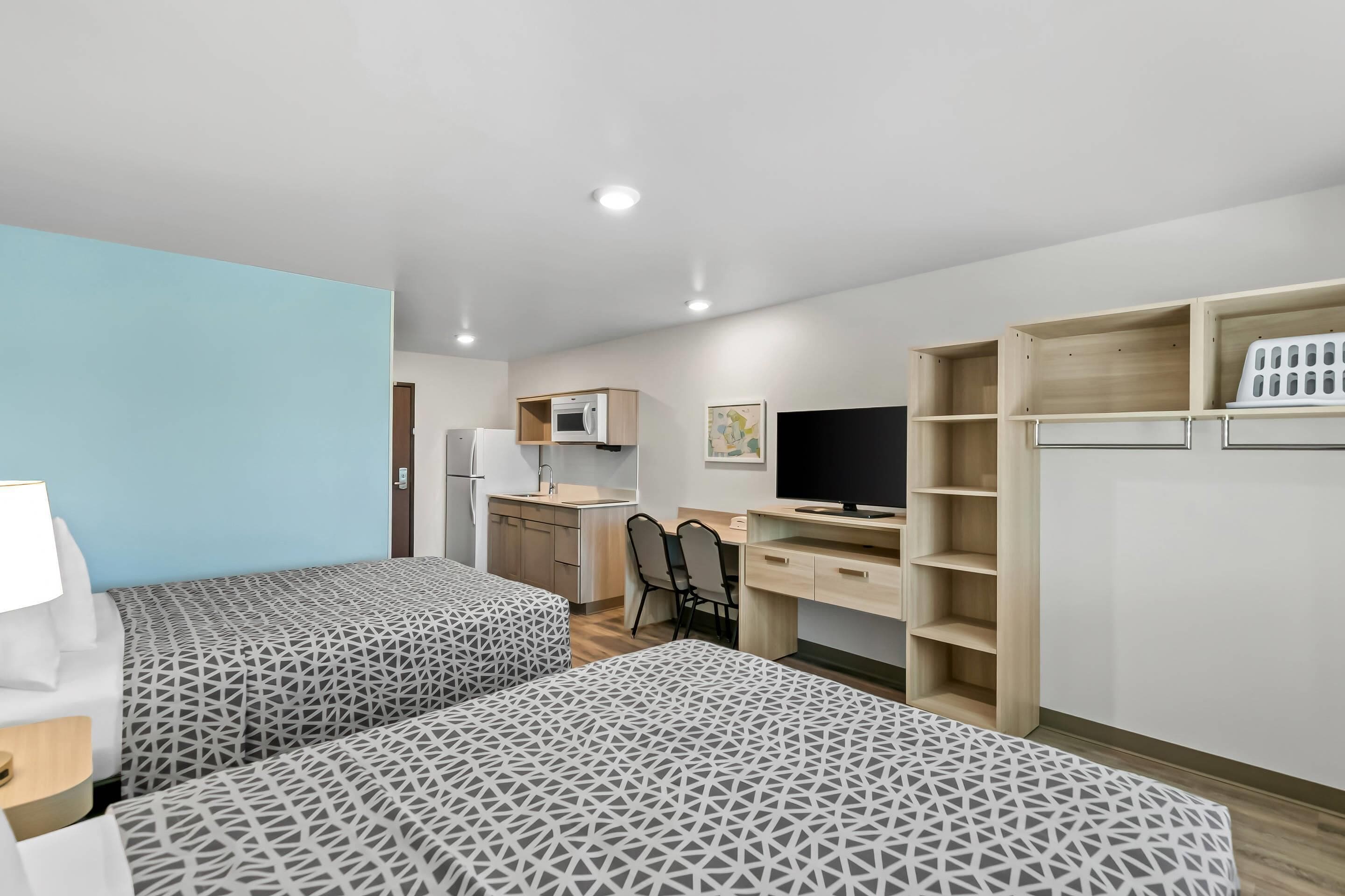 A hotel room with two beds, a desk, a chair, a TV, a microwave, and a wardrobe.