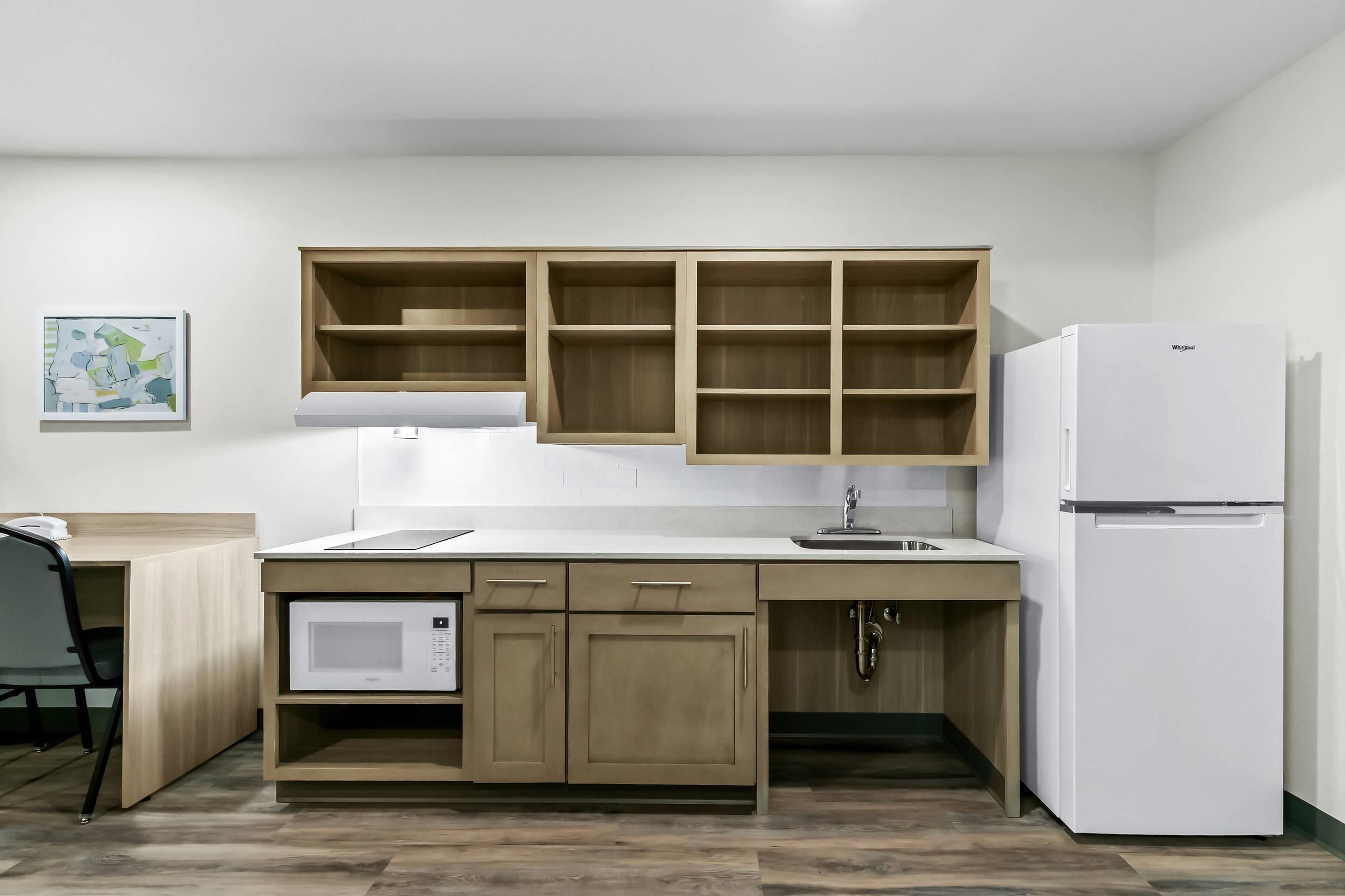 Una cocina compacta con armarios de madera, un microondas integrado y un refrigerador blanco.