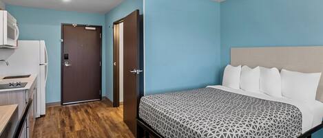 A bedroom with a bed, a desk, and a microwave.