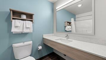 Un baño moderno con un inodoro blanco, un lavabo con un espejo encima y un estante con toallas.