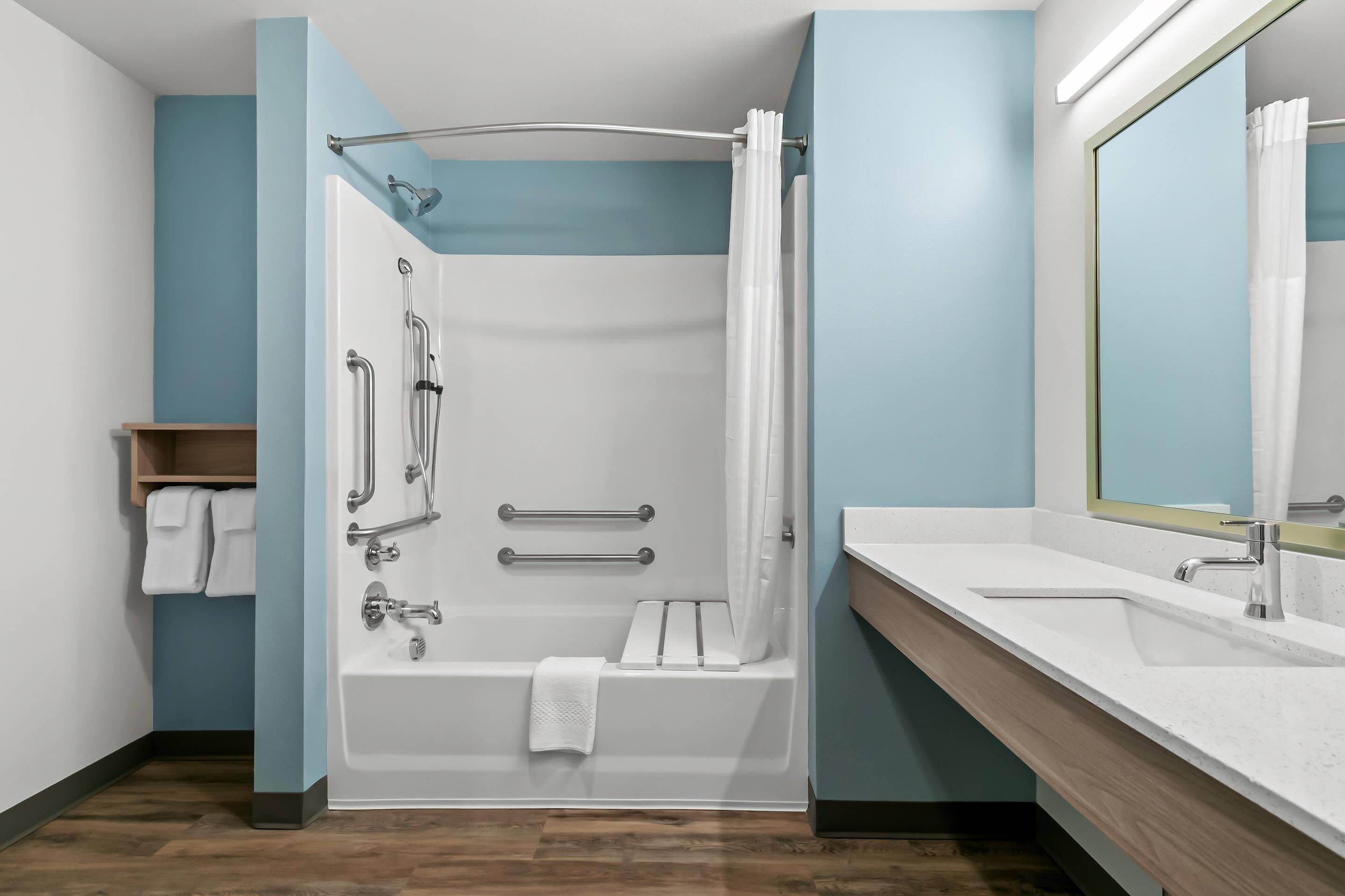 Un bagno moderno con doccia a filo pavimento, maniglie di sostegno, vasca da bagno e un mobile lavabo con specchio.