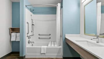 Un bagno moderno con doccia a filo pavimento, maniglie di sostegno, vasca da bagno e un mobile lavabo con specchio.