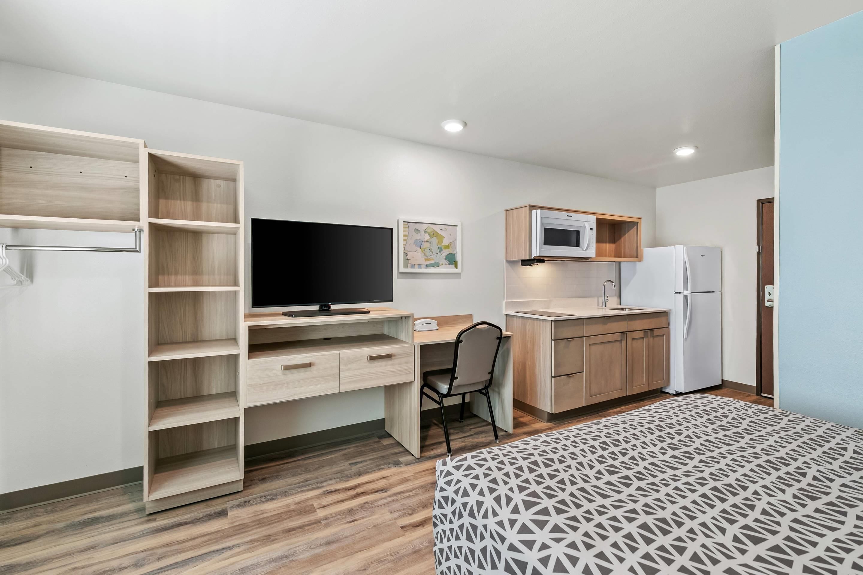 A compact room with a bed, a desk with a chair, a TV, a microwave, a refrigerator, and a wooden cabinet.