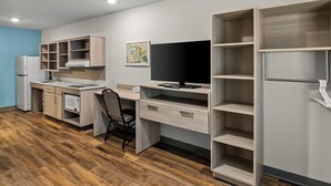 A modern kitchen with a built-in stove, a dining area with a chair, and a large open shelving unit. - Woodspring Suites Anderson North I-85 (Anderson)