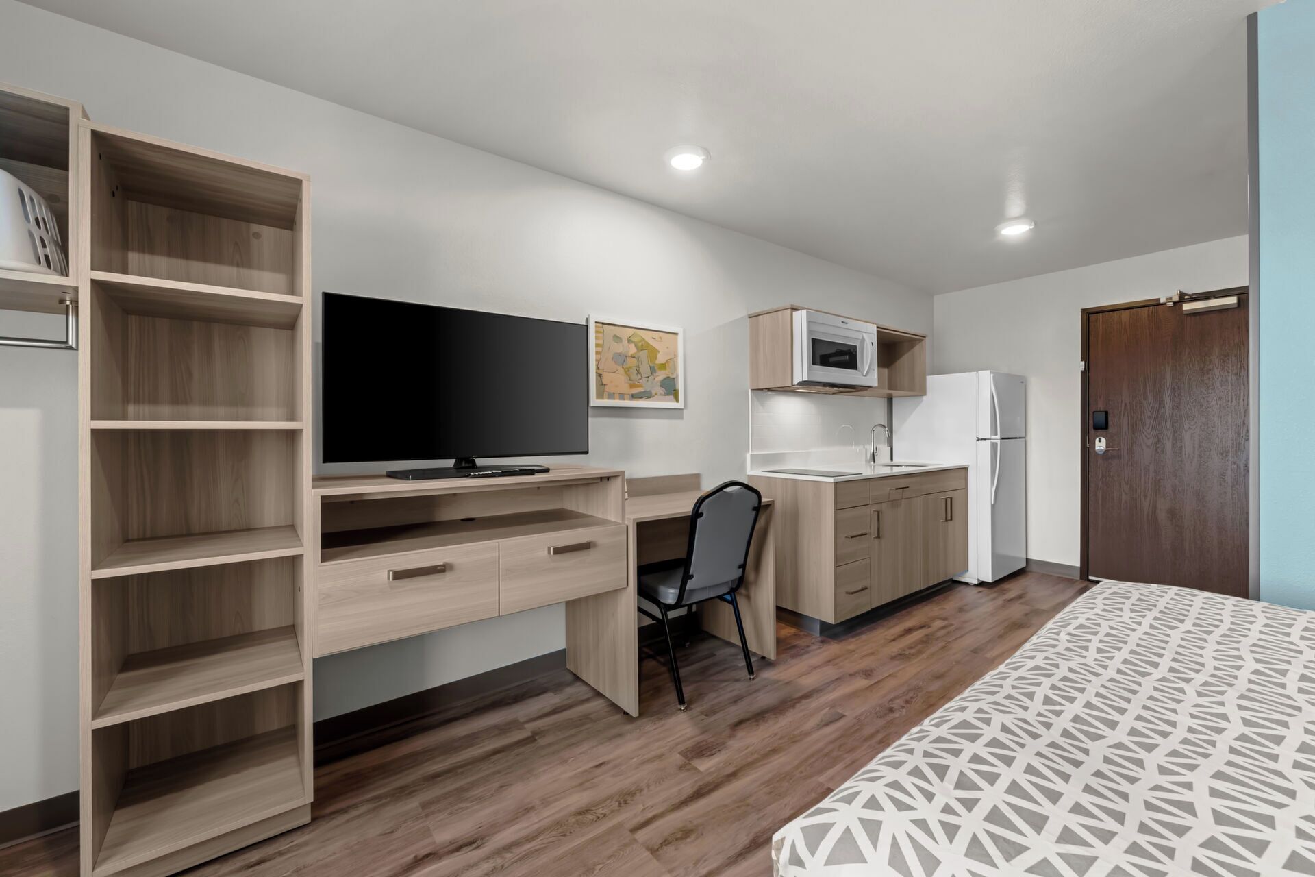 Ein gemütlicher Raum mit Holzschreibtisch, Fernseher, Mikrowelle, Kühlschrank und einem Bett mit gemustertem Überwurf.