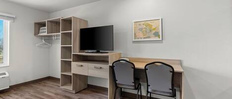 A modern room with a wooden desk, two chairs, a TV, and a shelving unit.