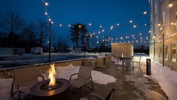 An outdoor patio area with string lights, a fire pit, and stone walls.