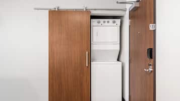 A compact laundry room with a white washer and dryer, wooden sliding doors, and a metal towel rack.
