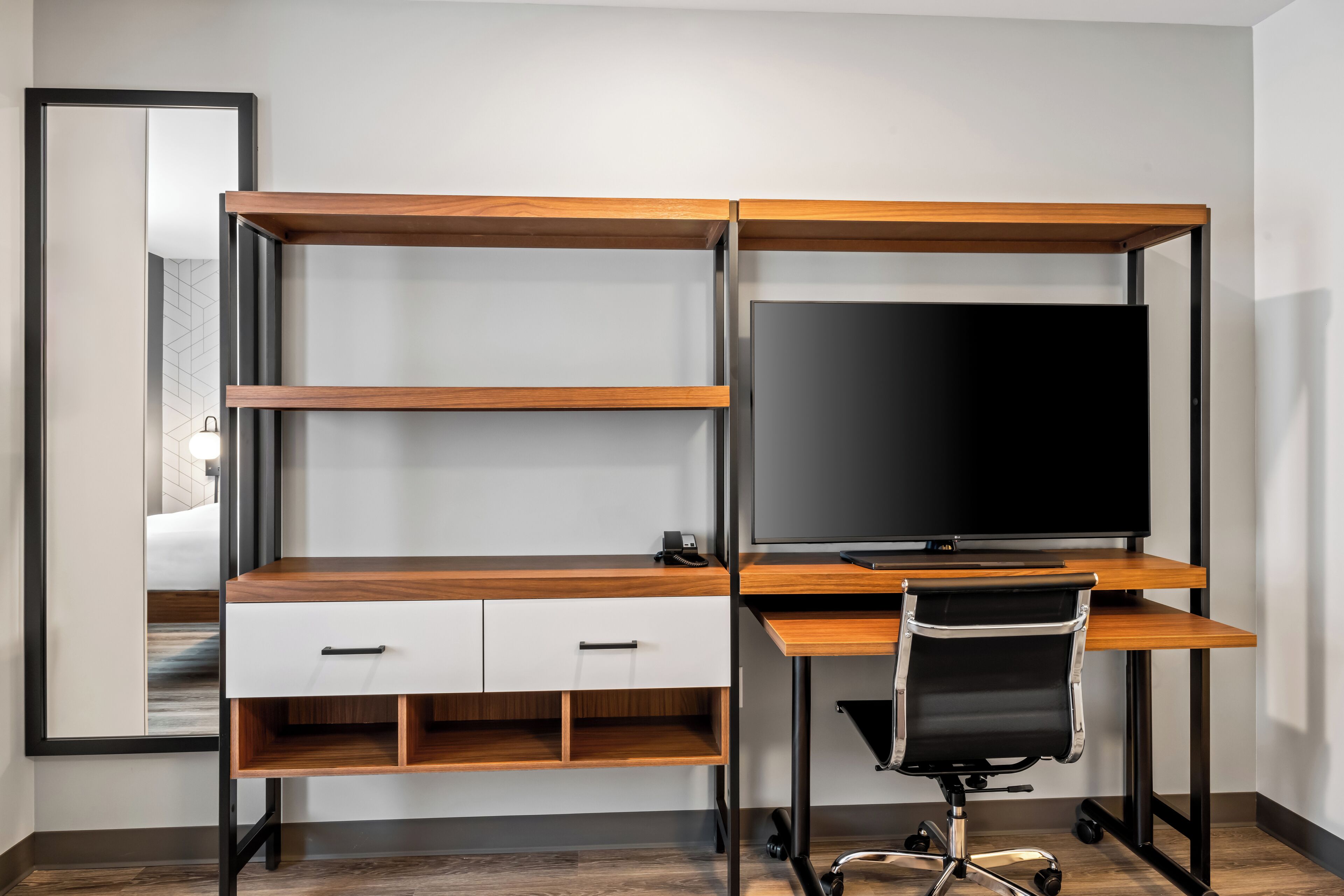 A modern office desk with a flat-screen TV, a chair, and a wooden desk with drawers and shelves.