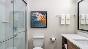 A modern bathroom with a glass shower enclosure, a white toilet, a framed abstract painting, and a vanity with a mirror.