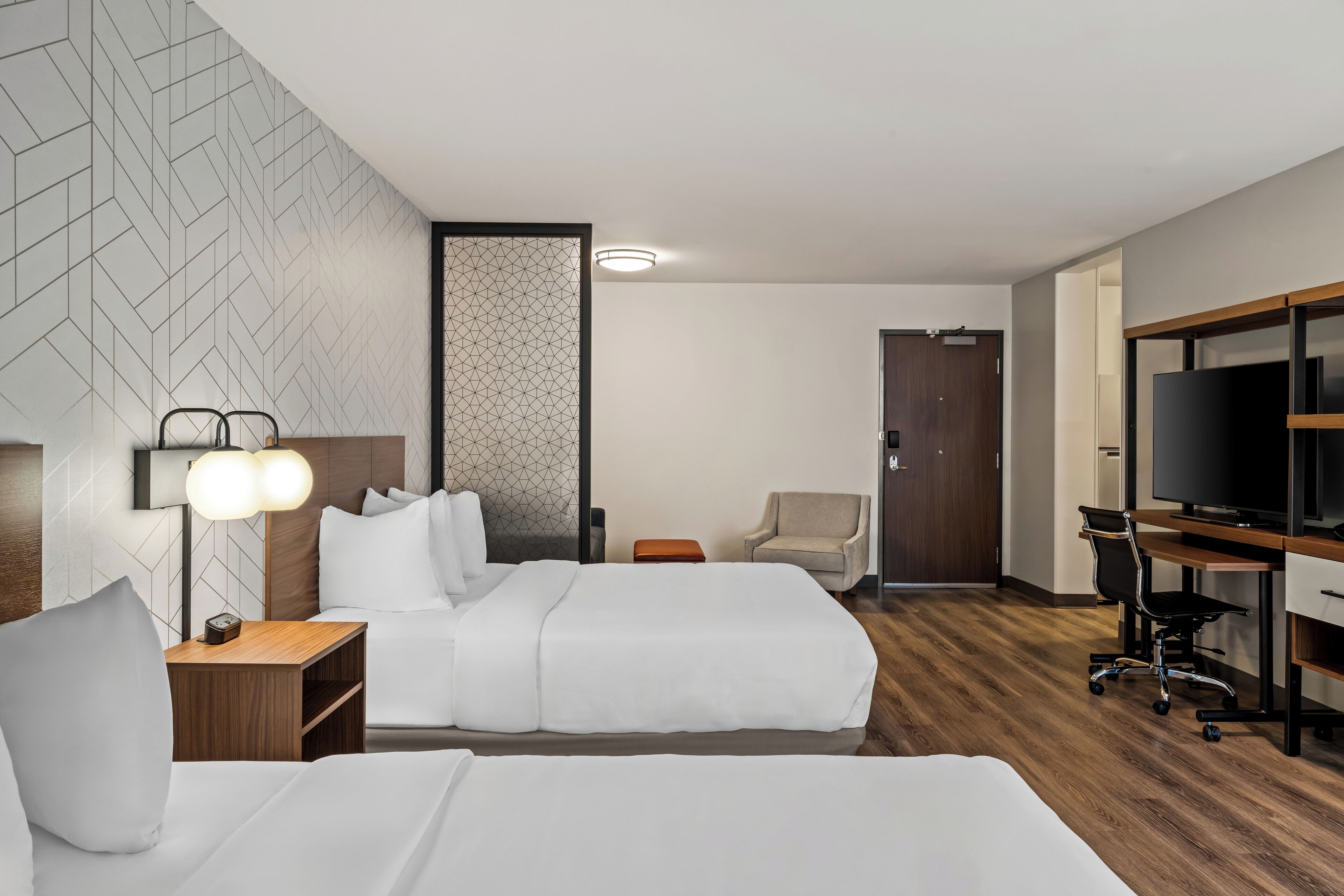 A hotel room with two beds, a desk with a computer, a TV, and a chair.