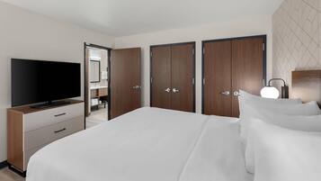 Habitación de hotel con una cama grande, televisión, armario y baño visible a través de una puerta abierta.