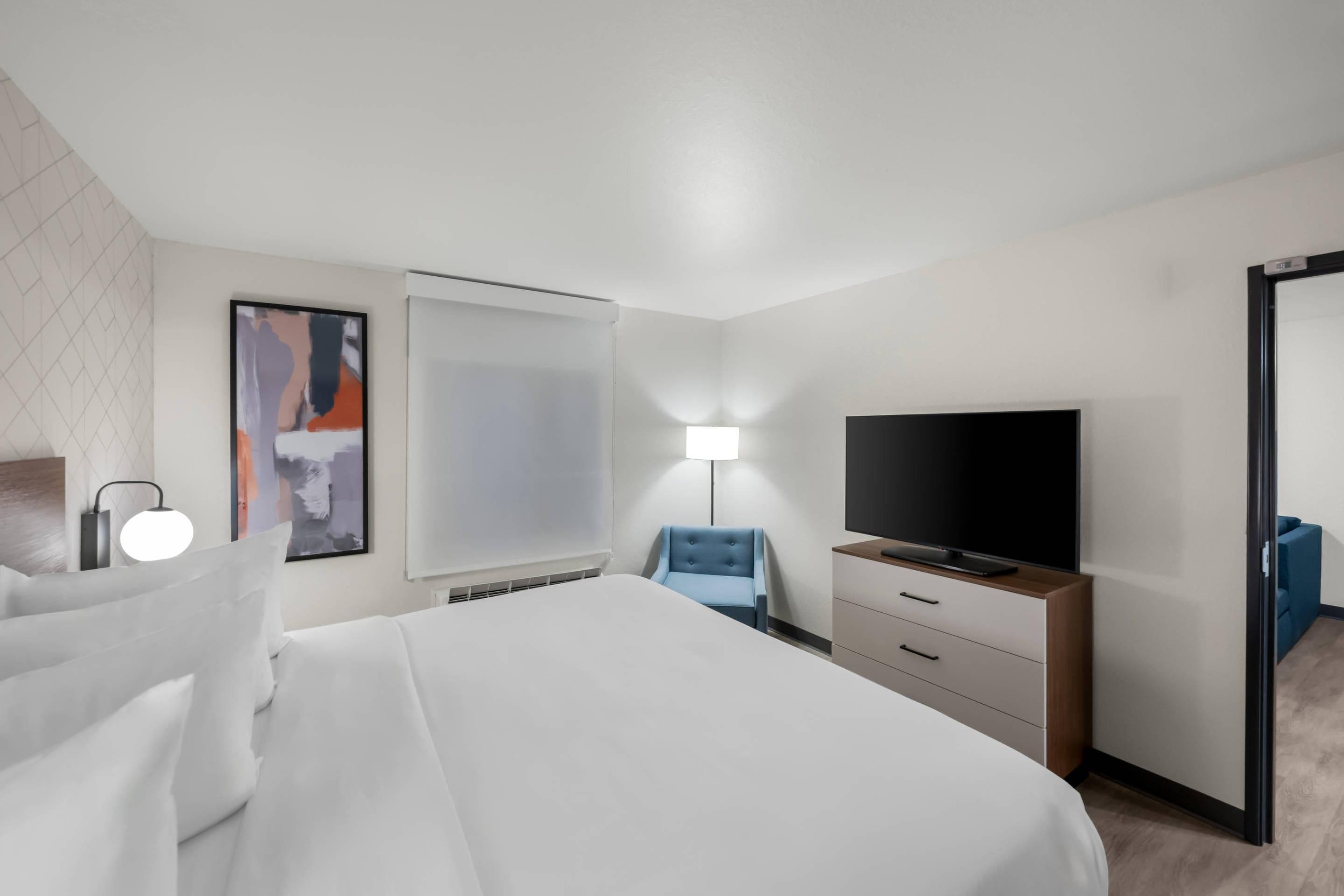 A modern hotel room with a large bed, a flat-screen TV, a desk, and a chair.