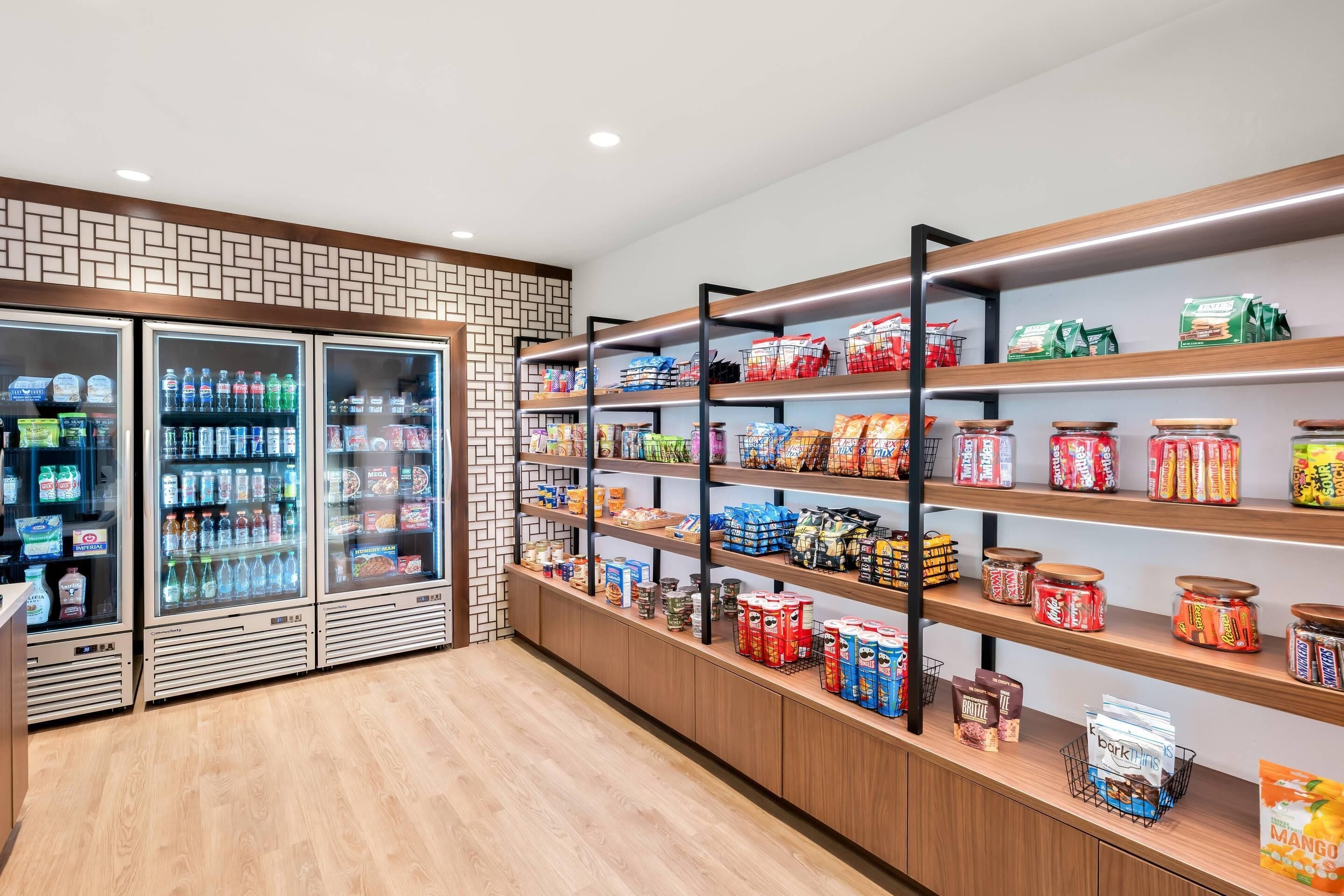 A well-lit snack and beverage area with refrigerated drinks and shelves stocked with various snacks and packaged goods.