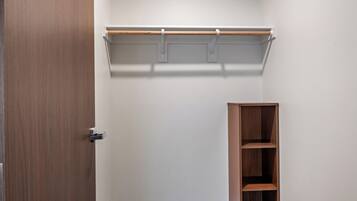 Una habitación con puerta de madera, pared blanca, estantería de madera y un banco negro.