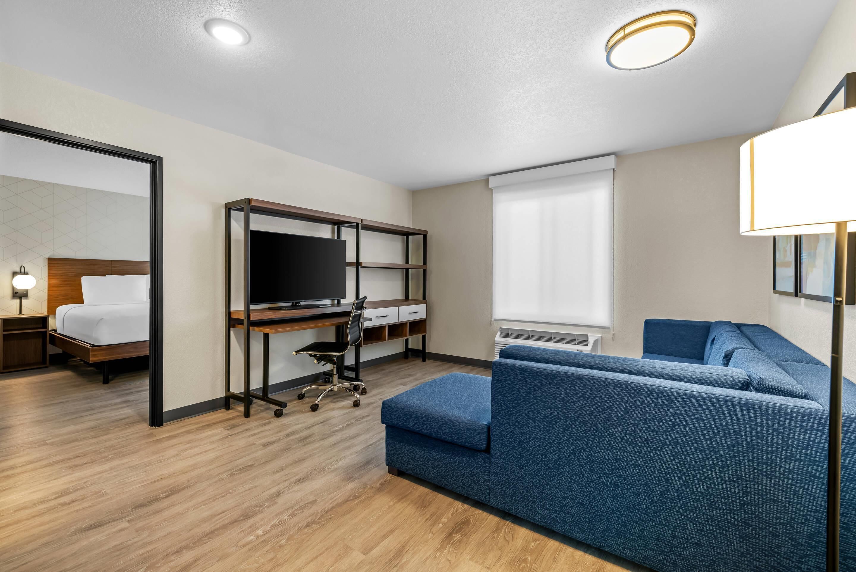 Habitación de hotel con cama, escritorio con computadora, sofá y televisor.