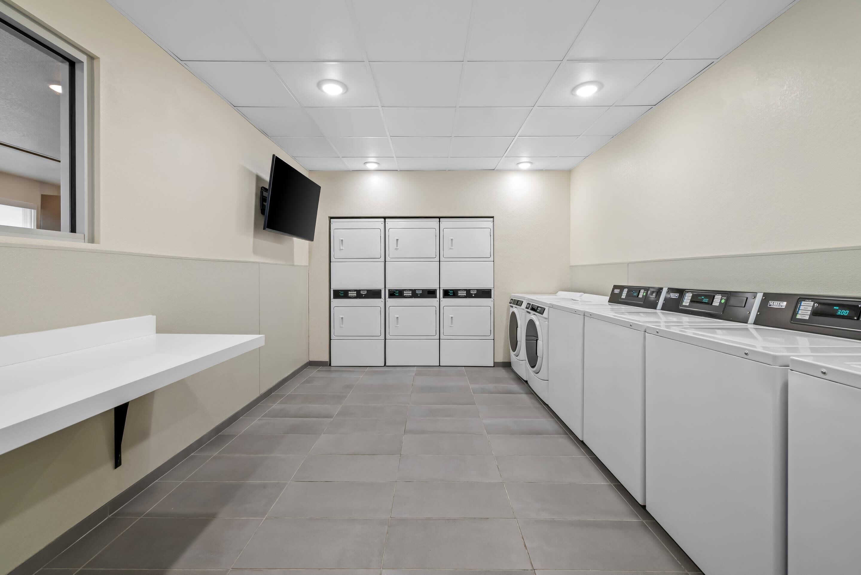 A laundry room with a white sink, three washing machines, and a flat-screen TV on the wall.