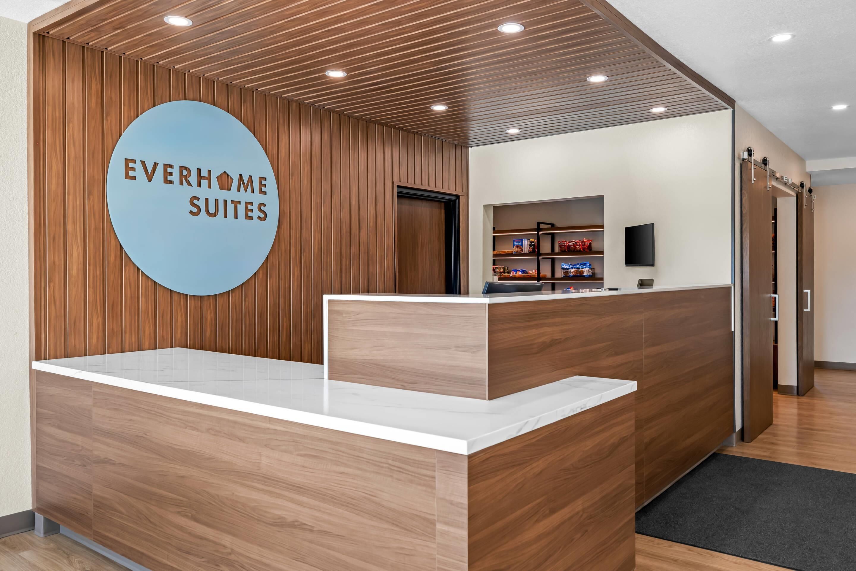 Un mostrador de recepción con detalles de madera y un letrero azul que dice "EVERHOME SUITES".