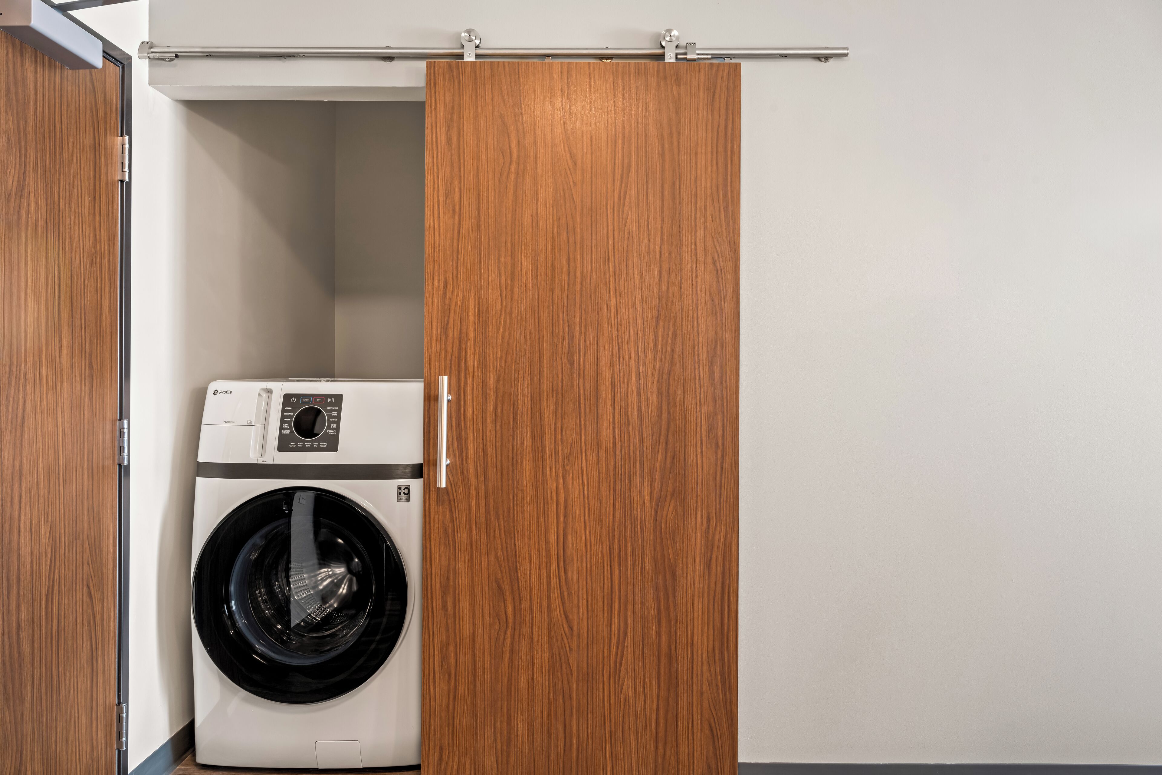 A compact laundry room with a front-loading washing machine and a wooden wardrobe.