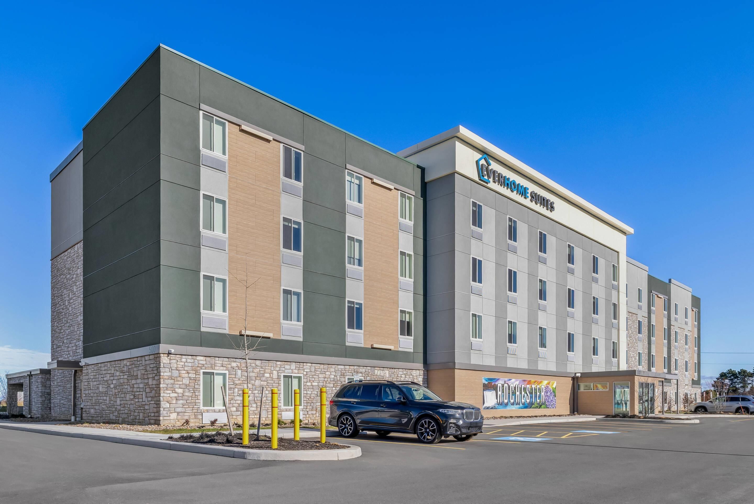 A modern hotel building with a sign reading "COVENTRY SUITES" and a parking lot with a BMW SUV.