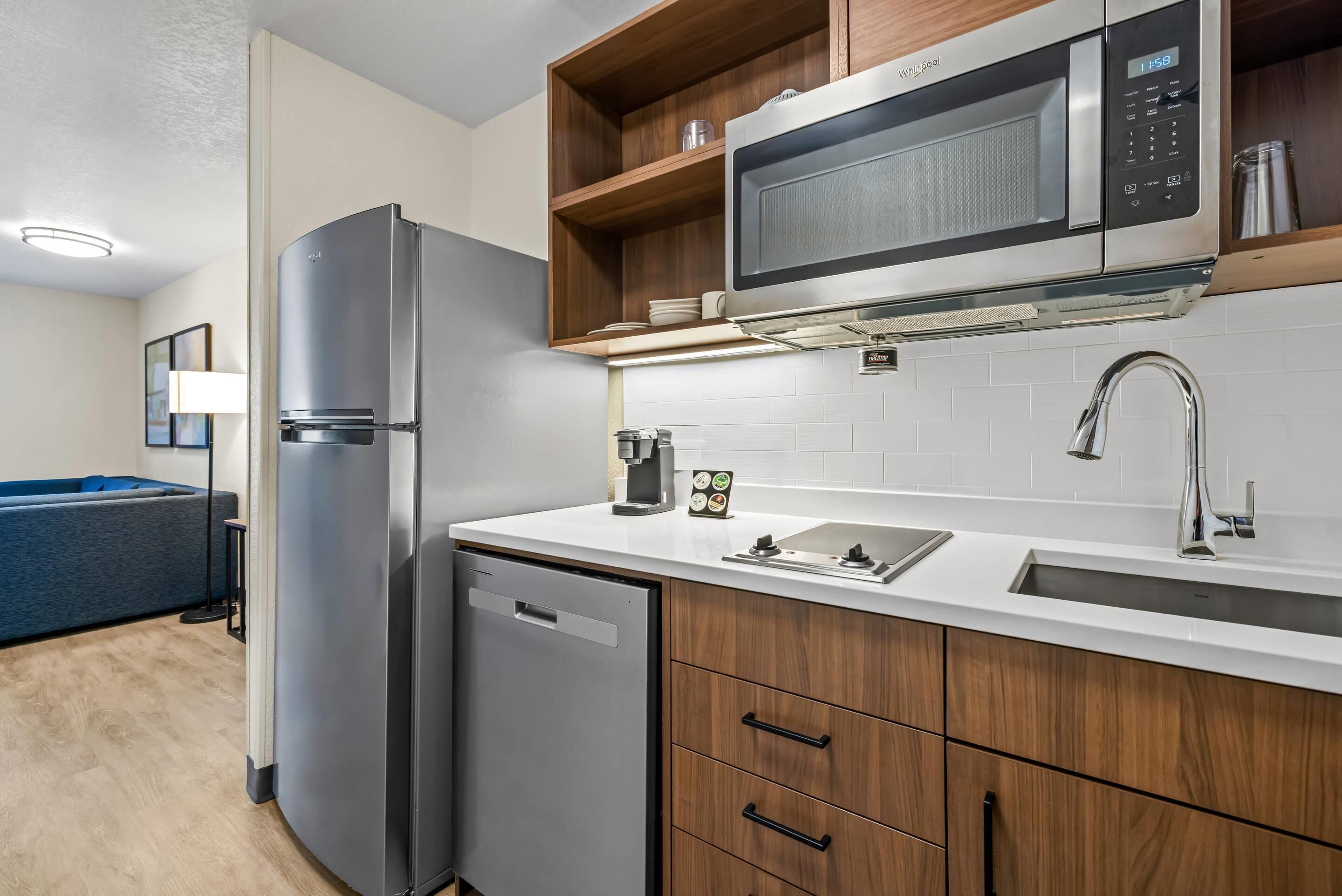 A compact kitchen with a built-in microwave, a stainless steel refrigerator, and wooden cabinets.