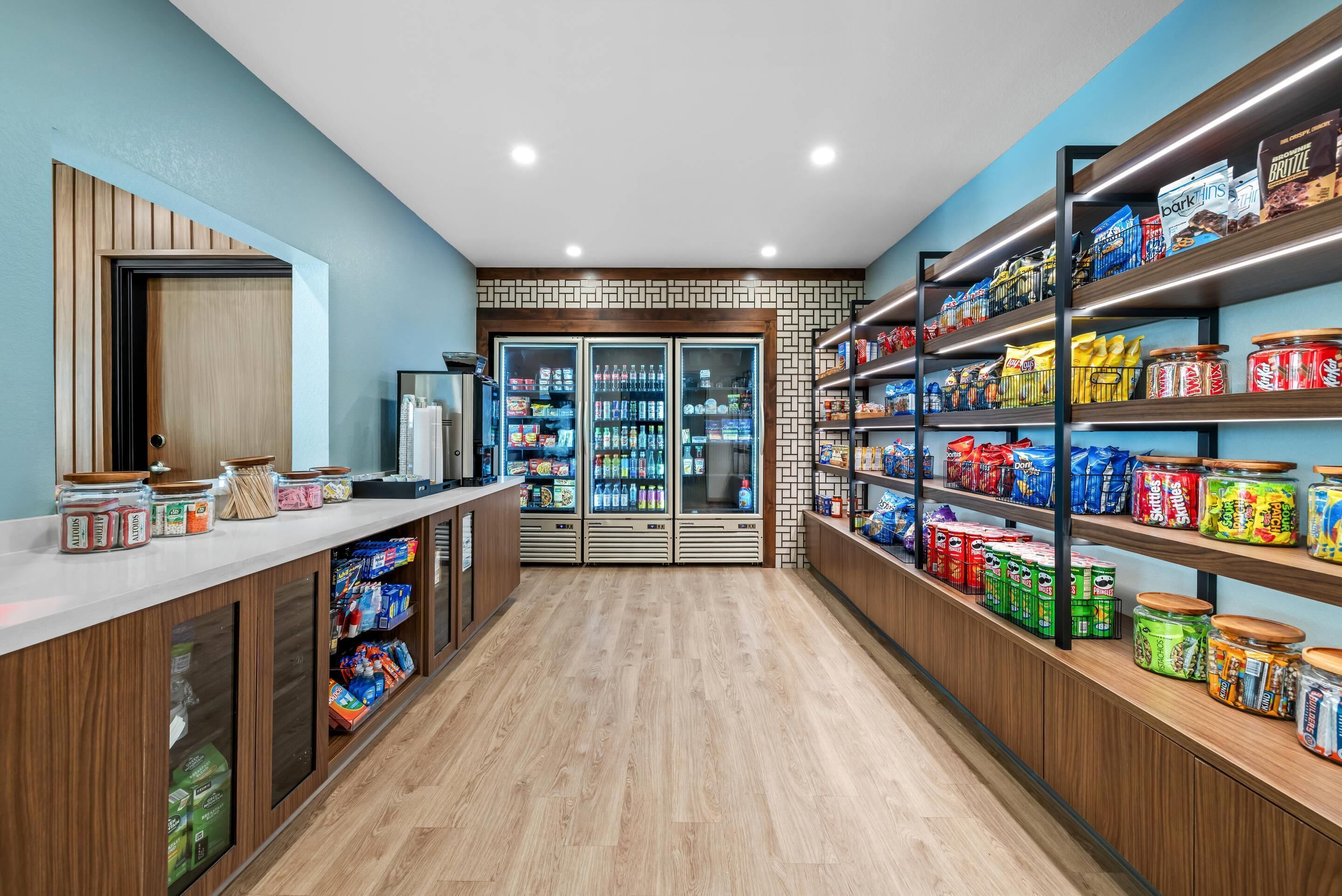 A well-lit store with wooden floors and shelves stocked with snacks and beverages.