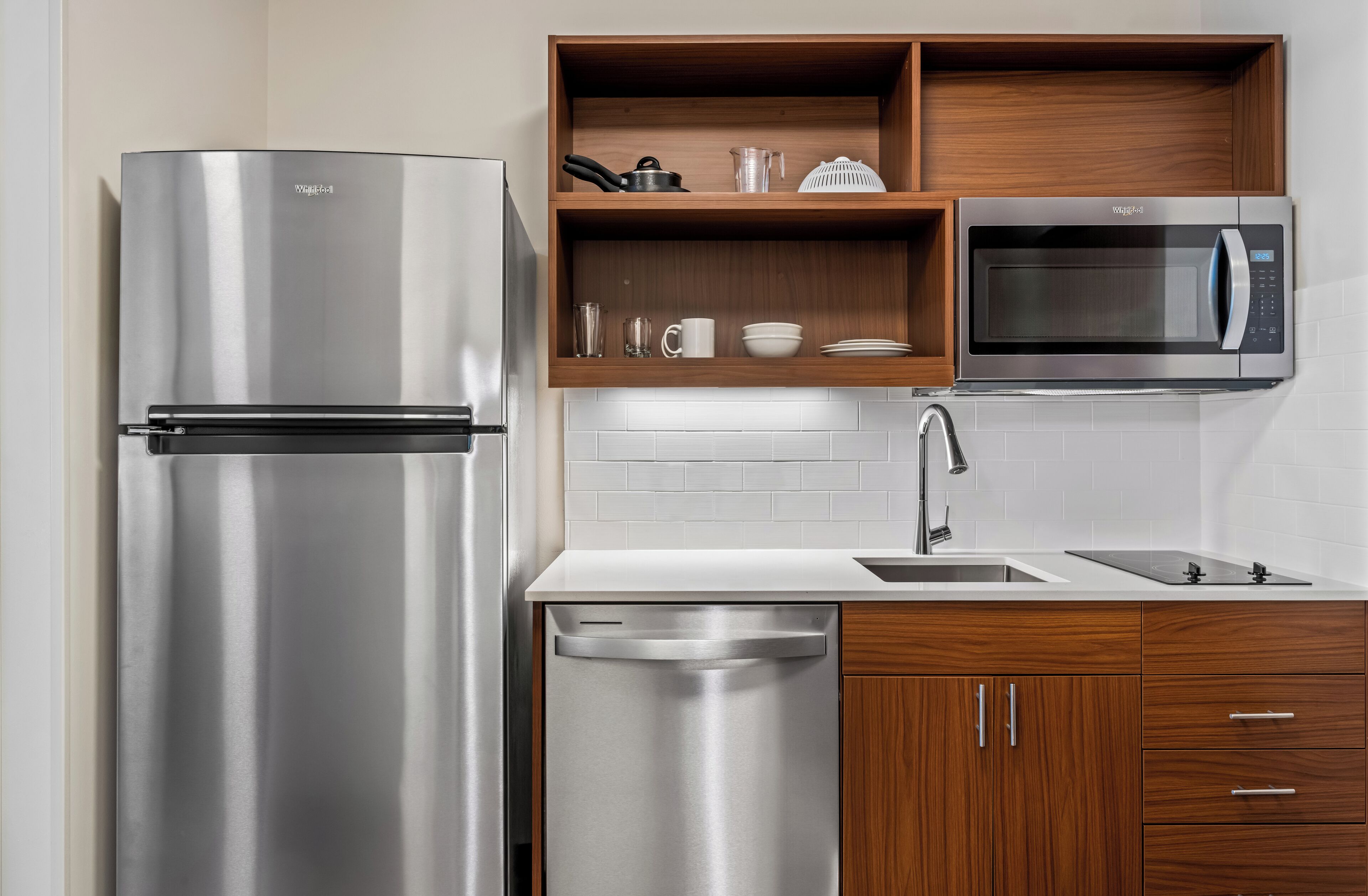 A modern kitchen with a stainless steel refrigerator, a built-in microwave, and wooden cabinets.
