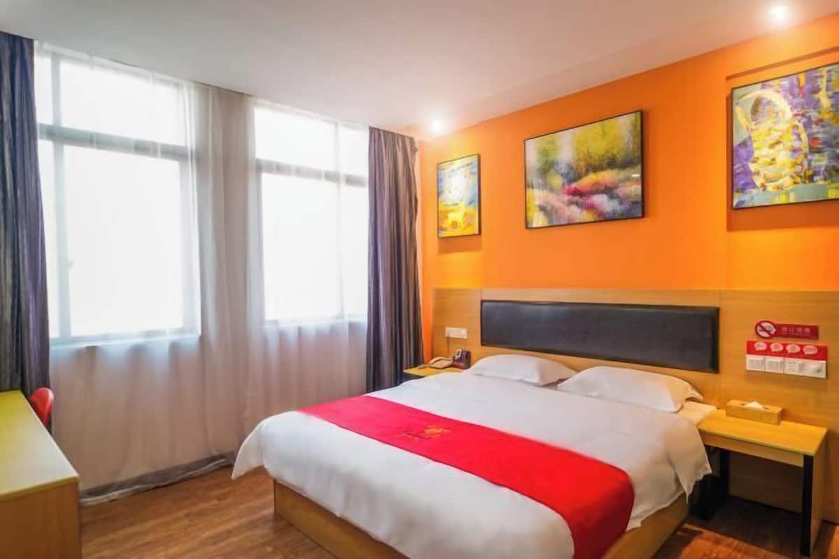 A hotel room with a large bed, a nightstand, a desk, and a window with curtains.