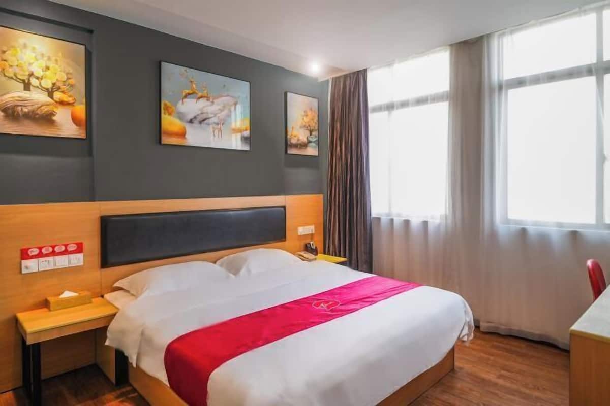 A hotel room with a large bed, a wooden headboard, a nightstand, and a desk.