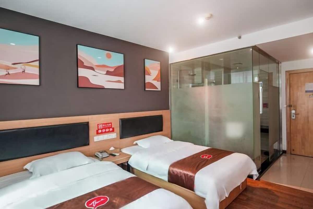 A hotel room with two beds, a glass shower enclosure, and artwork on the wall.