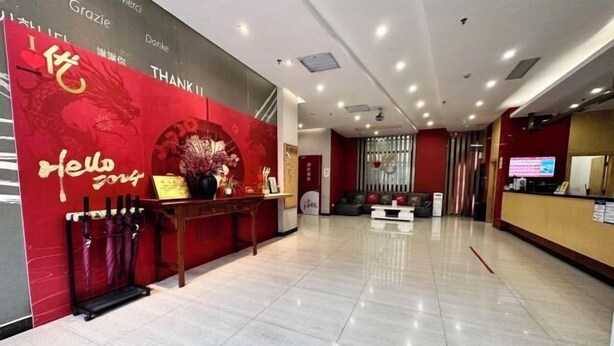A hotel reception area with a red wall, a reception desk, and a seating area. - Shankee Hotel (Maoming High-Speed Railway Station 1959 Cultural and Creative Pedestrian Street) (Maoming)
