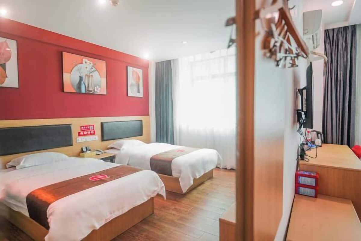 A hotel room with two beds, a desk, and a TV.