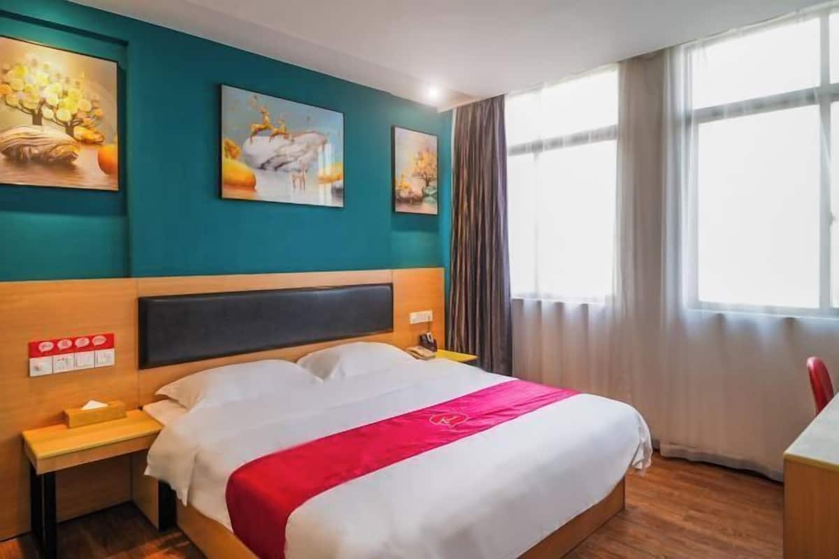 A hotel room with a bed, a nightstand, a desk, and a window with curtains.