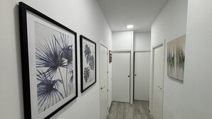 A hallway with framed botanical prints on the walls, a wooden floor, and white doors at the end.