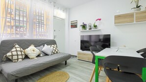 A modern living room with a grey sofa, a TV, a dining table with chairs, and a window with curtains.