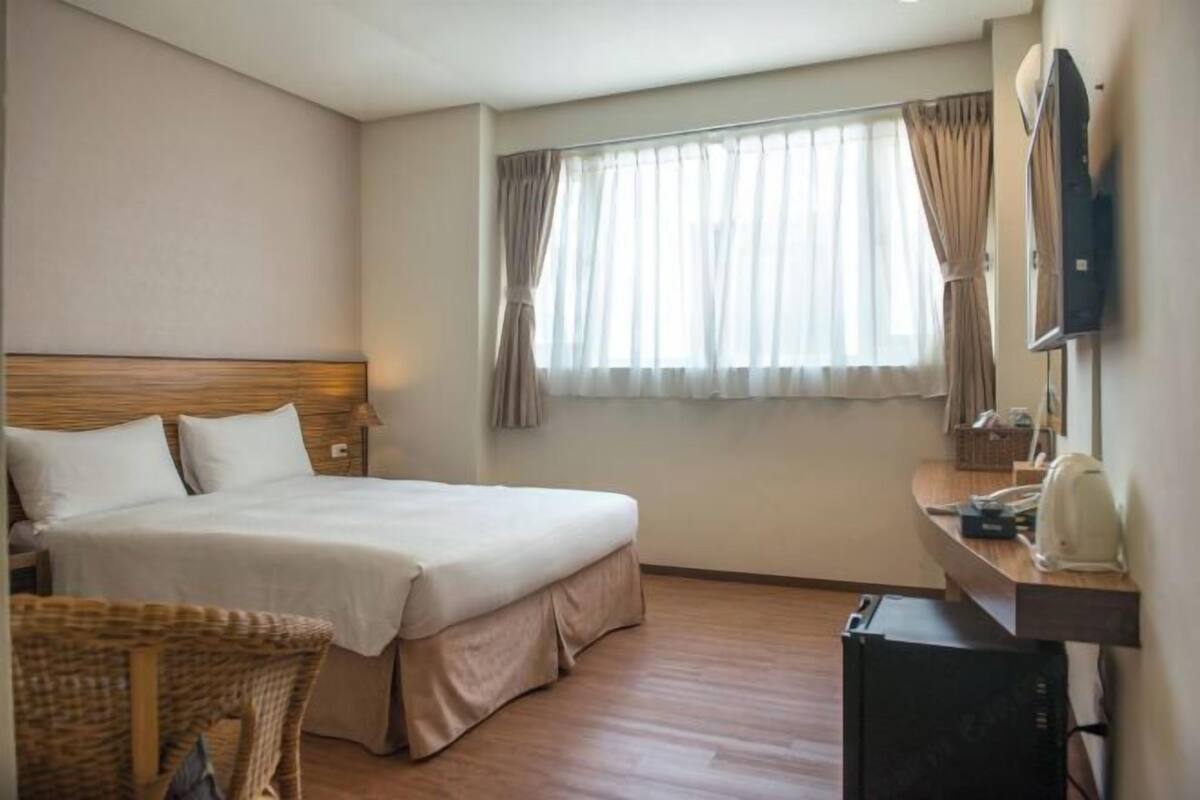 Una habitación de hotel con cama, televisión, escritorio y ventana con cortinas.