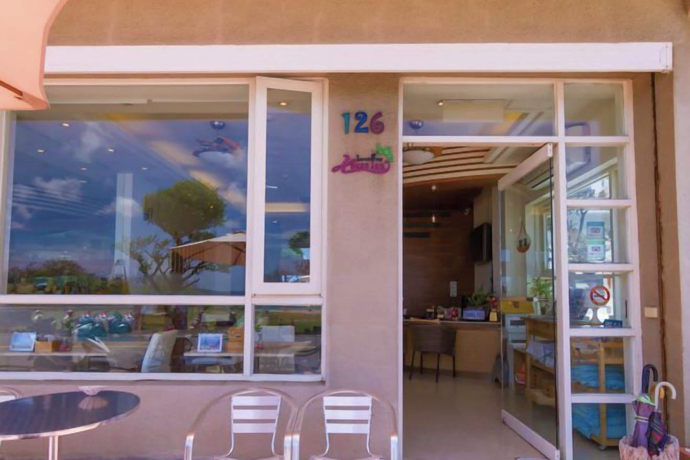 Une devanture de magasin avec de grandes vitrines, le numéro « 126 » inscrit sur le mur, et une table avec des chaises à l’extérieur.