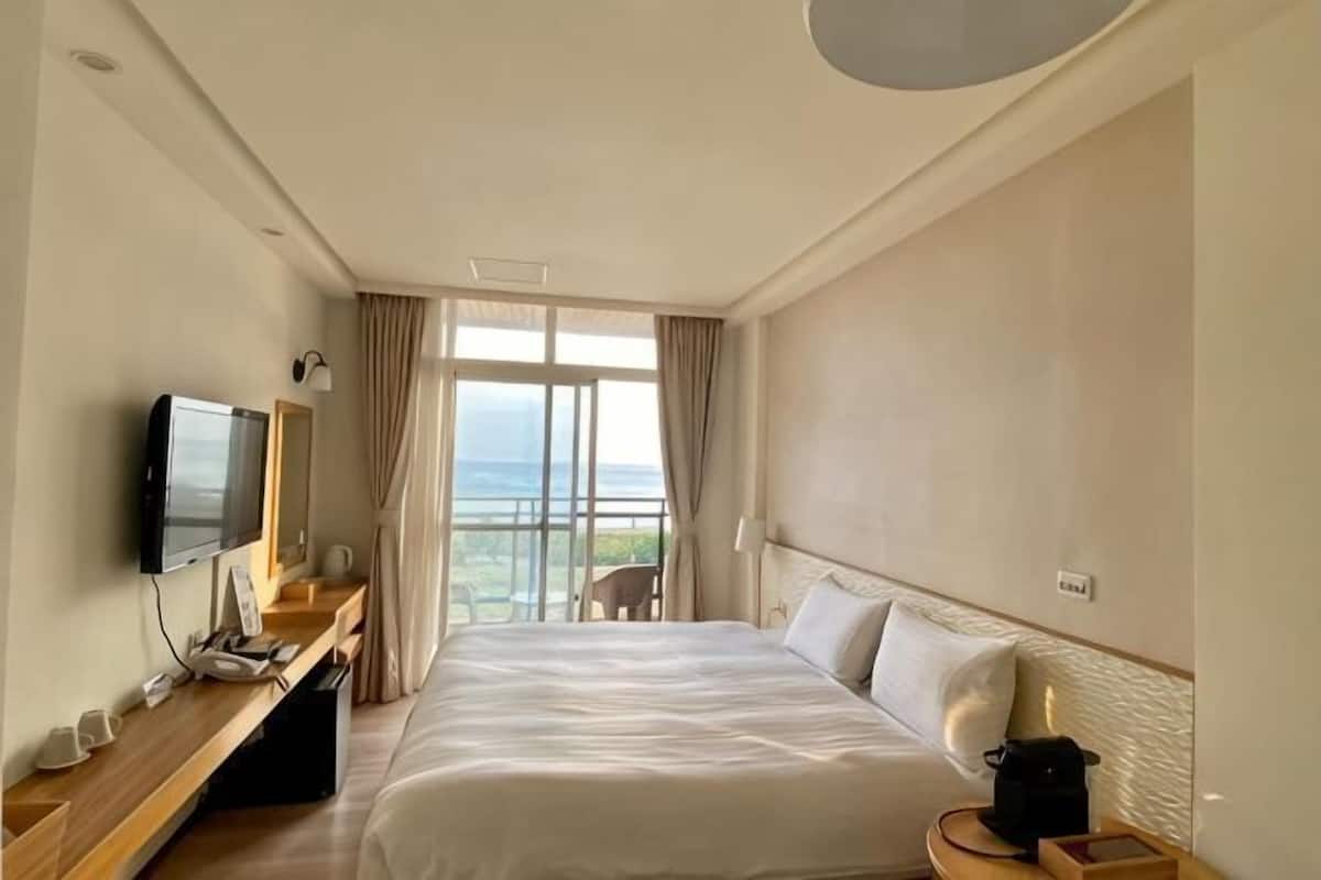 Habitación de hotel con cama, televisor, escritorio, silla y vista al exterior.